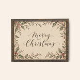 A framed Christmas sign with the words “Merry Christmas” in black script, surrounded by a vintage-style floral border with green leaves and red berries on a warm cream background.