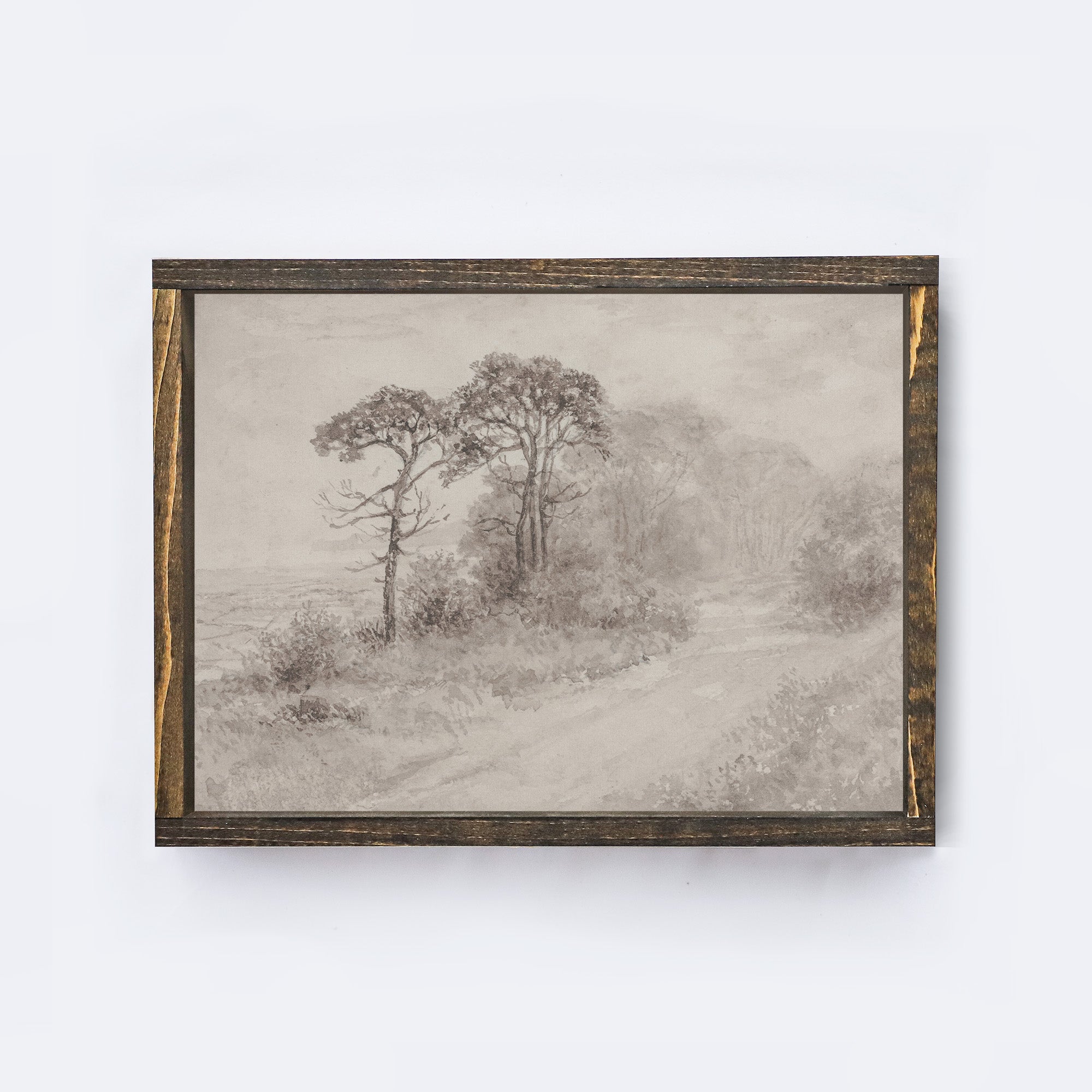 Framed artwork of a landscape with trees on a wooden shelf against a white wall.