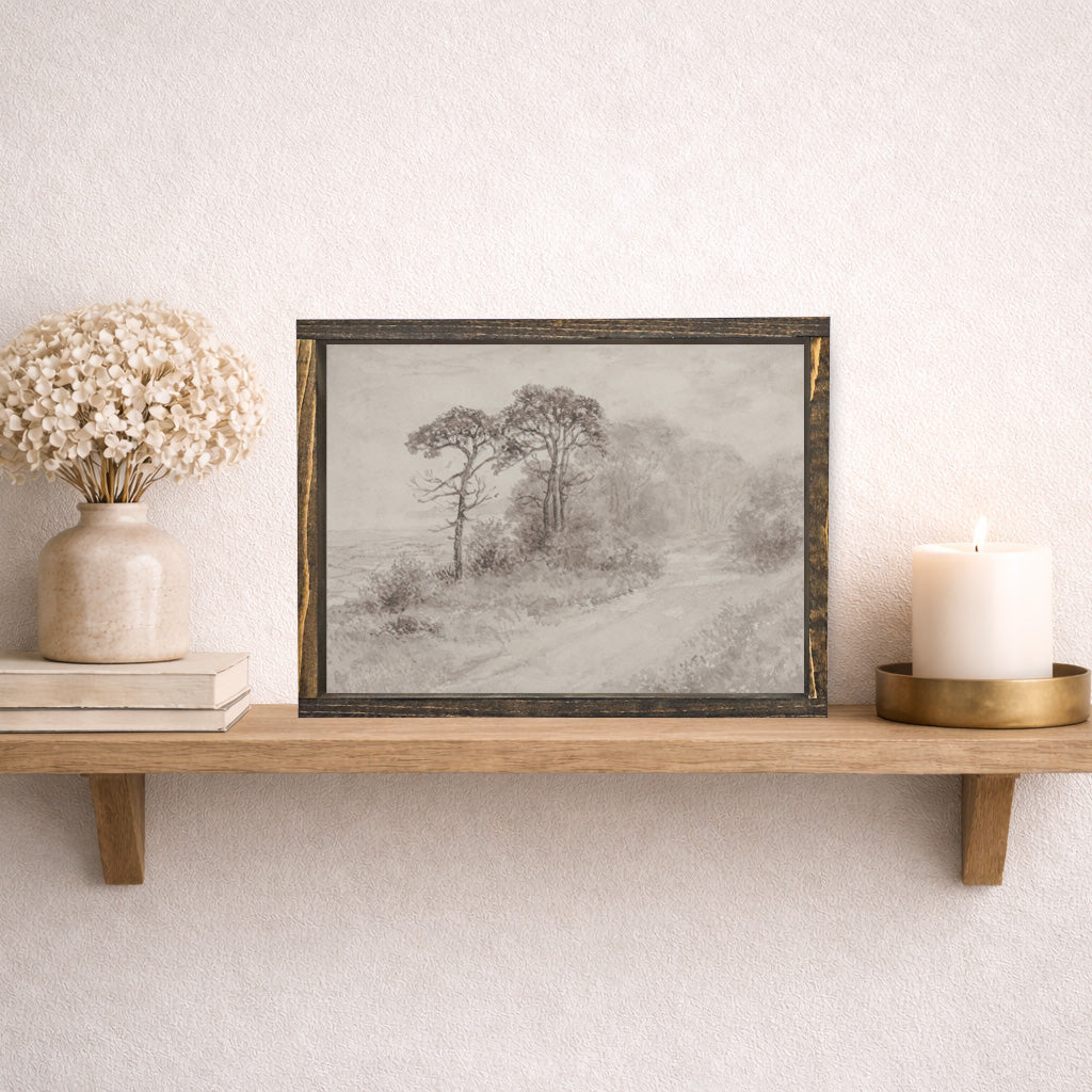 Framed artwork of a landscape with trees on a wooden shelf against a white wall.