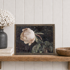 Framed artwork of a rose on a wooden shelf with decorative items.