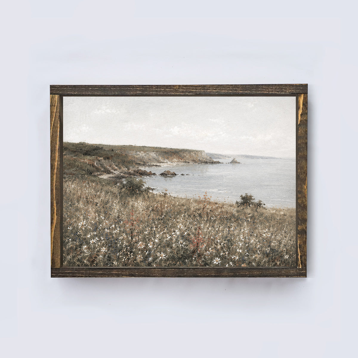 Framed landscape print of a coastal scene with a wooden frame on a white wall.